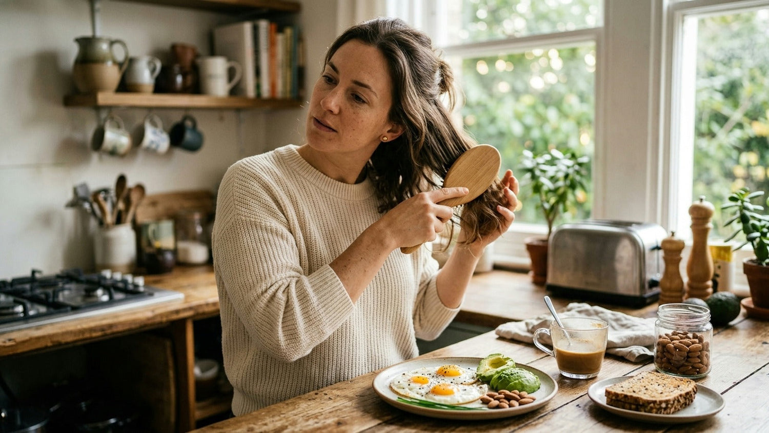 An adult woman brushes her hair beside a breakfast of eggs, avocado, and almonds.