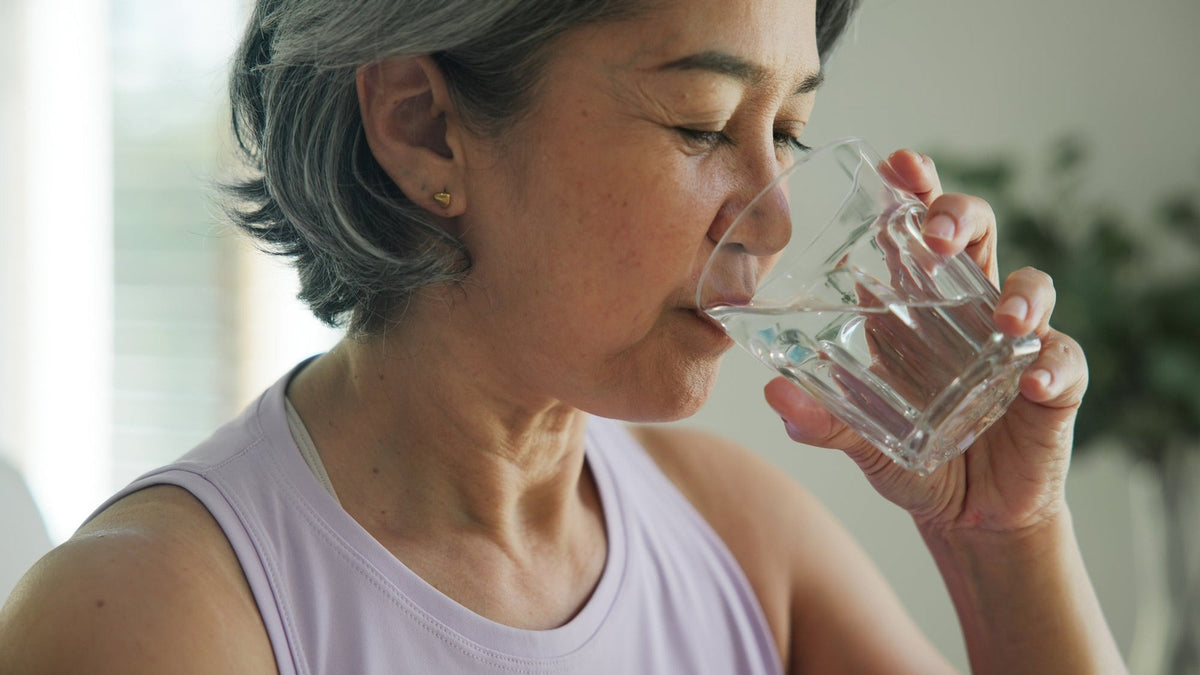 Older woman drinking a glass of water at home, part of a once-daily nattokinase dosage routine